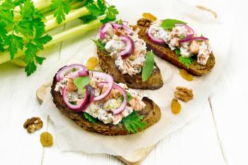 Salad of salmon, petiole celery, raisins, walnuts, red onions and cottage cheese on toasted bread with green lettuce on paper on a light wooden board background
