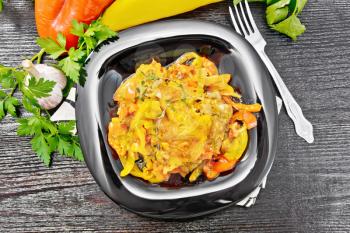 Chicken stewed with tomatoes, yellow and red bell peppers and cheese in a plate on napkin, thyme, parsley and garlic on black wooden board background from above