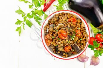 Green lentils stewed with eggplant, tomatoes, garlic and spices in a bowl on a kitchen towel, parsley on wooden board background from above