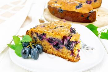 Piece of sweet cake with black grapes and honey, mint and a fork in a plate, a towel on light wooden board background