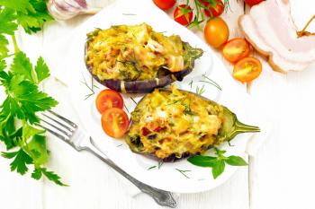 Stuffed eggplants with smoked brisket, tomatoes, onions, carrots with garlic, cheese and herbs in a plate on a kitchen towel on a background of light wooden board on top