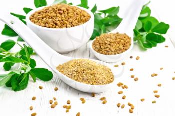 Ground fenugreek in a spoon, spice seeds in a bowl and spoon with leaves on wooden board background