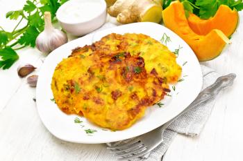 Pumpkin fritters in a plate on napkin, sour cream in a bowl, parsley, garlic and ginger on wooden board background