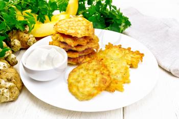 Pumpkin and Jerusalem artichoke fritters with sour cream in a plate, napkin, parsley on wooden board background