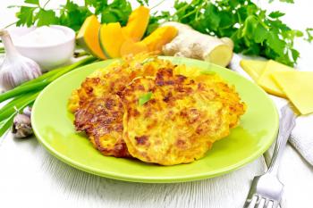 Pumpkin, cheese and ginger fritters in a green plate, sour cream in a bowl, napkin, parsley and fork on white wooden board background