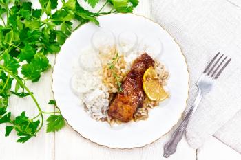Salmon with sauce of honey, lemon juice, garlic, hot pepper and soy sauce, boiled rice, lemon and thyme in a plate, parsley, towel and fork on the background of wooden board on top