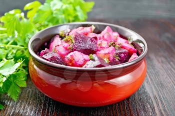 Beetroot and potato salad, seasoned with vegetable oil and vinegar in a bowl, parsley on a wooden board background
