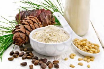 Cedar flour in a bowl, nuts and cones, a spoon with peeled nuts, green pine branch and cedar milk in a bottle on wooden board background