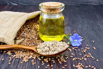 Flaxseed flour in a spoon, oil in a glass jar, blue linen flower, brown seeds in a bag on a dark wooden board background