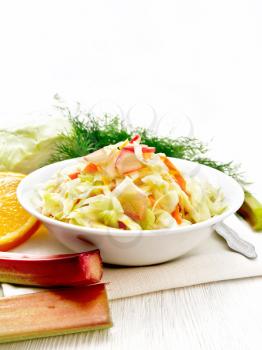 Fresh cabbage, carrot and rhubarb salad with orange juice, honey and mayonnaise dressing in a plate on a towel, dill and fork on wooden board background