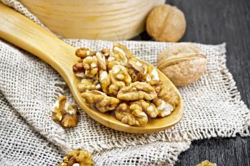 Walnuts peeled in a spoon on burlap, whole nuts in a bowl on background of dark wooden board