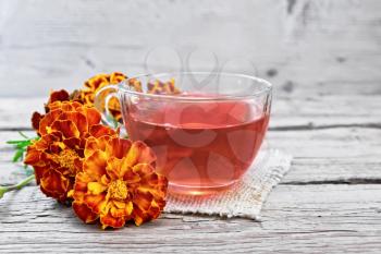 Marigold herbal tea in a glass cup, fresh flowers on a sackcloth napkin on a wooden board background