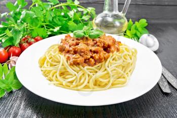 Spaghetti pasta with Bolognese sauce of minced meat, tomato juice, garlic, wine and spices in a plate, vegetable oil, spicy herb on a dark wooden board background