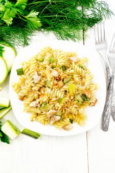 Fusilli pasta with chicken breast, zucchini, cream and pine nuts in a plate, fork and parsley on the background of a light wooden board on top