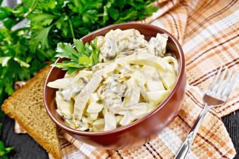 Salad with squid, egg and champignons in a bowl on a towel, bread, fork and parsley on wooden board background