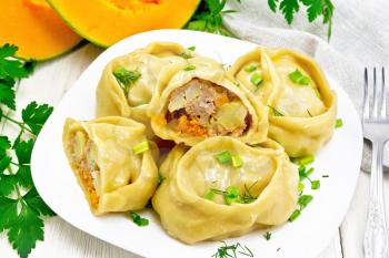 Manty steamed pies with minced meat and pumpkin, green onions in a plate, towel, parsley and fork on background of light wooden board