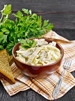Salad with squid, egg and champignons in a bowl on a towel, bread, fork and parsley on dark wooden board background