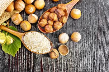 Hazelnut flour in a spoon, nuts in a bag, spoon and on the table, filbert branch with green leaves on the background of wooden board from above
