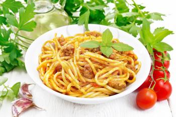 Spaghetti pasta with sauce Bolognese of minced meat, tomato juice, garlic, wine, spices and basil in a plate, vegetable oil, spicy herb on a light wooden board background