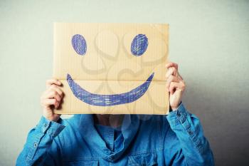Curly man with a kraft cardboard instead of a head, a cheerful smiley. On a gray background.