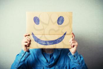 Curly man with a kraft cardboard instead of a head, a cheerful smiley. On a gray background.