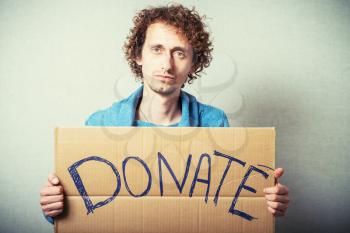 Curly man with a kraft cardboard with text donate help. On a gray background.