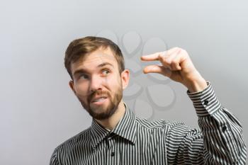 Young handsome man show a little bit. Gesture. On a gray background