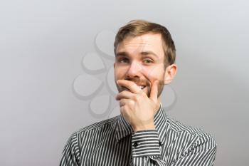 Young handsome man covered her mouth in surprise. Gesture. On a gray background