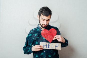 Closeup portrait of worried young man holding a help and a heart ! Human emotion facial expression