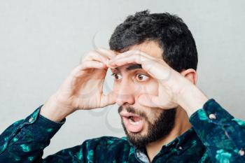 Shocked man  looking through hands, making binoculars