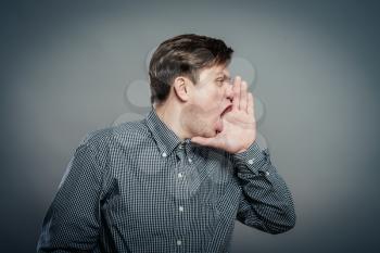 Closeup side view profile portrait, angry upset young man, worker, employee, business man, hand to mouth, open mouth yelling, isolated white background. Negative emotion facial expression emotion