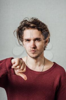 young man showing thumbs down on a gray background