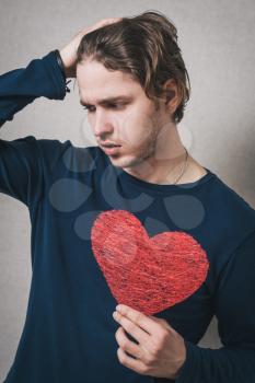 A sad man with a red heart. Gray background.