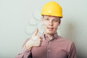 Construction worker in yellow hard hat. Happy male in his 20s. Young man portrait with thumbs up.