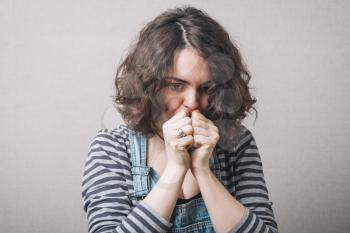 Sad woman looking down holding fists near his mouth. Gray background