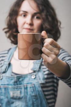 A woman offers a cup of coffee or tea. Gray background