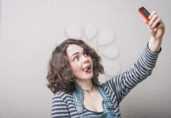 Woman playfully makes selfie on the phone, a grimace. Gray background
