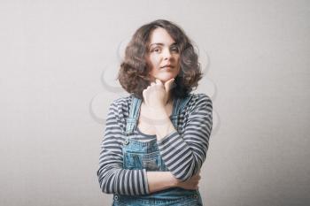 Woman thinking with hand on chin. On a gray background.