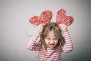 sweet little girl holds a valentines heart and thinks of love, isolated on gray background