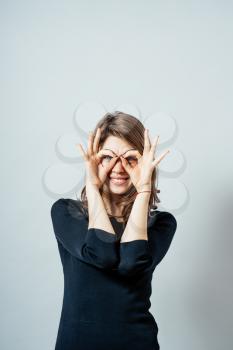 Young happy woman holding her hands over her eyes as glasses and  looking through fingers