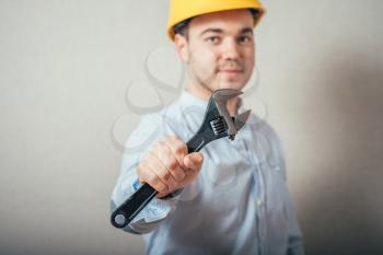 The man in yellow helmet with a wrench. On a gray background.