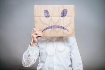 Putting a smiling face on. Man holding cardboard paper with smiley face printed on as sadness sorrow.