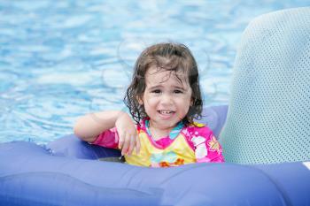 Baby girl having fun on a blue float into a tropical swimming pool 