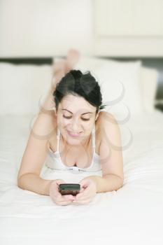 Happy female teenager using cellphone lying on the bed against white background 
