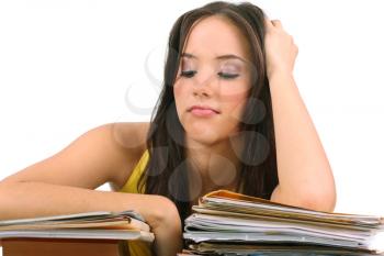 Stressed young woman sitting at a table among books and papers on a white background 
