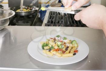 Italian food. Chef putting parmesan over a rigatoni with vegetables.