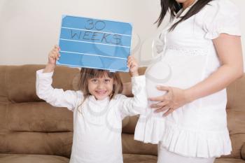 Girl holding a 30 weeks sign to her expectant mother