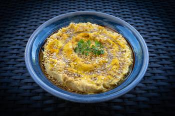 Tasty hummus (or houmous) in blue bowl on dark background