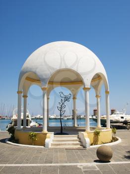 Mandraki harbour embankment pavilion with decorative iron tree and bird inside. Rhodes, Greece.