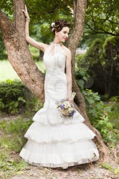 Young bride with bouquet near tree in the park
